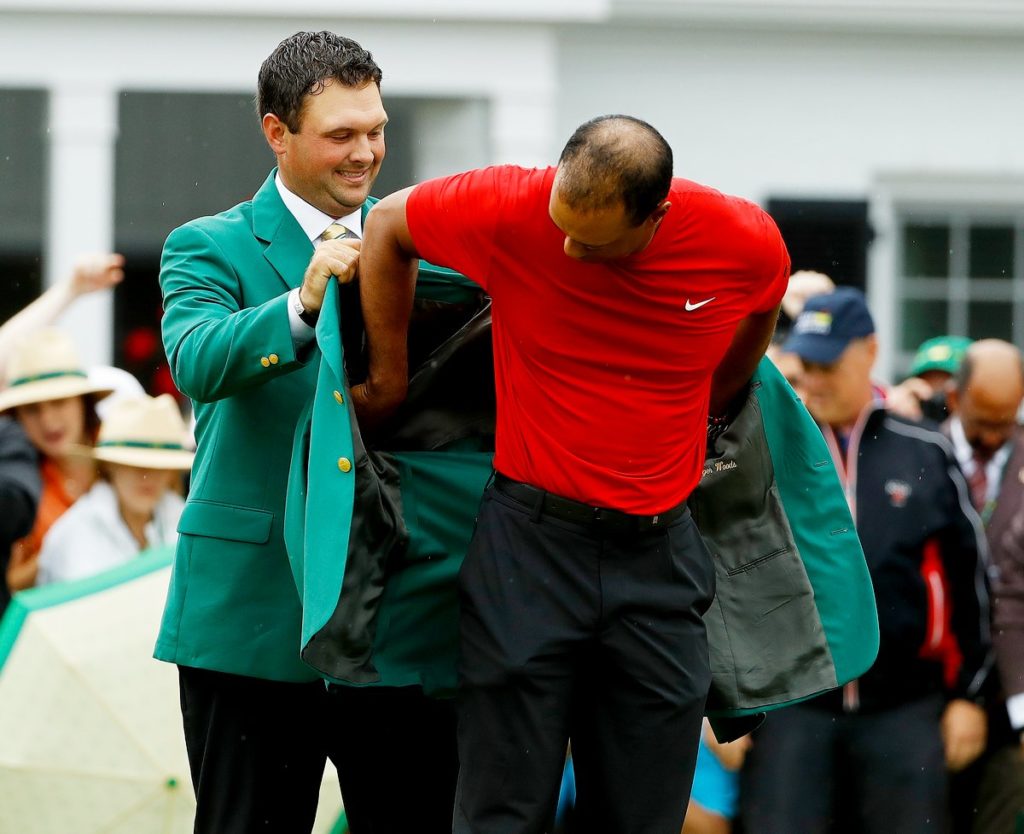 Patrick Reed, the 2018 Masters champions, helps Tiger Woods with his green jacket