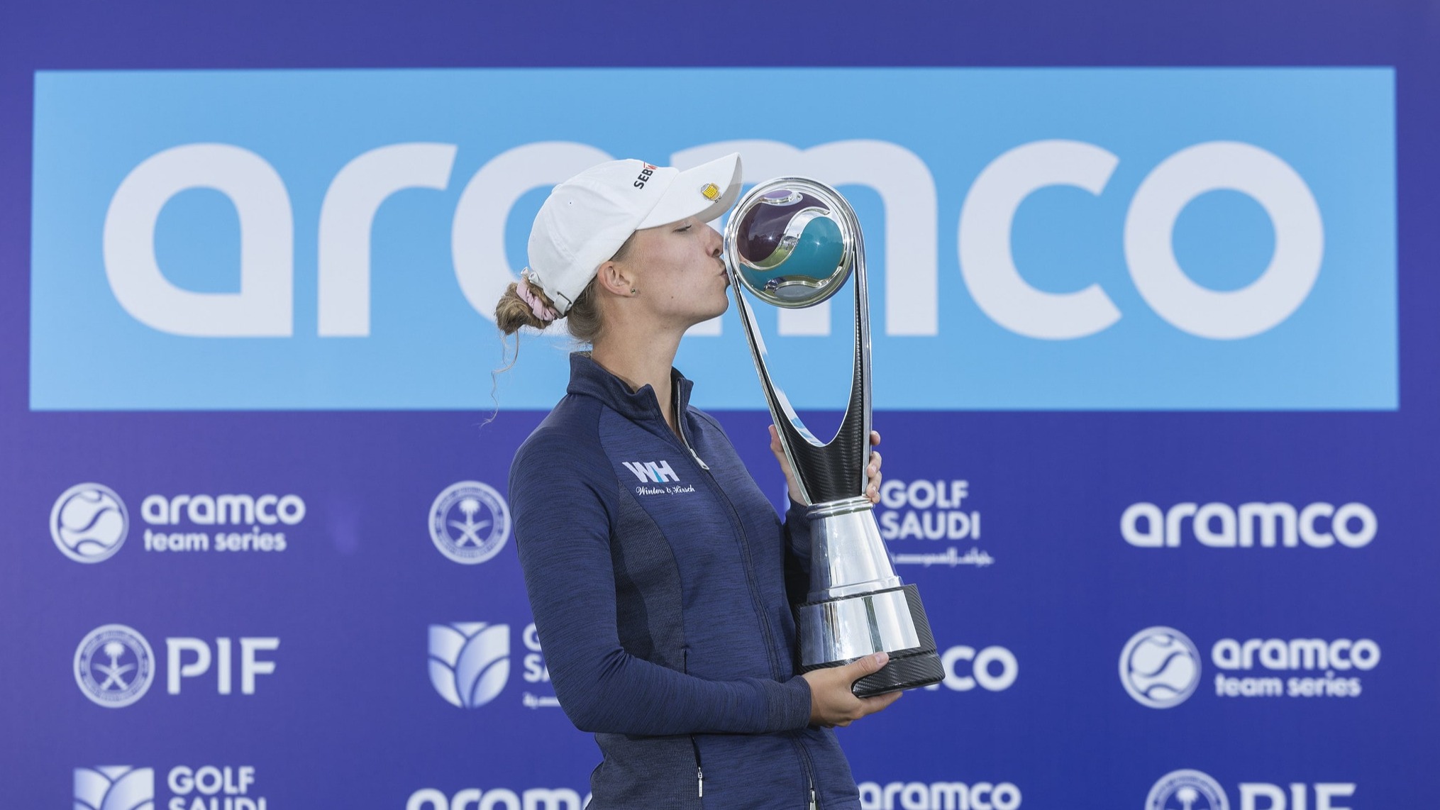 Alexandra Försterling holding the Aramco Team Series trophy against the sponsors board.