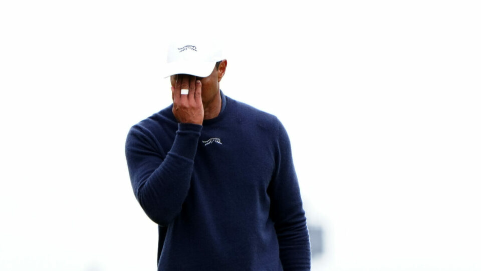 Tiger Woods covers his face with his right hand while holding his putter in his left