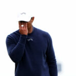 Tiger Woods covers his face with his right hand while holding his putter in his left